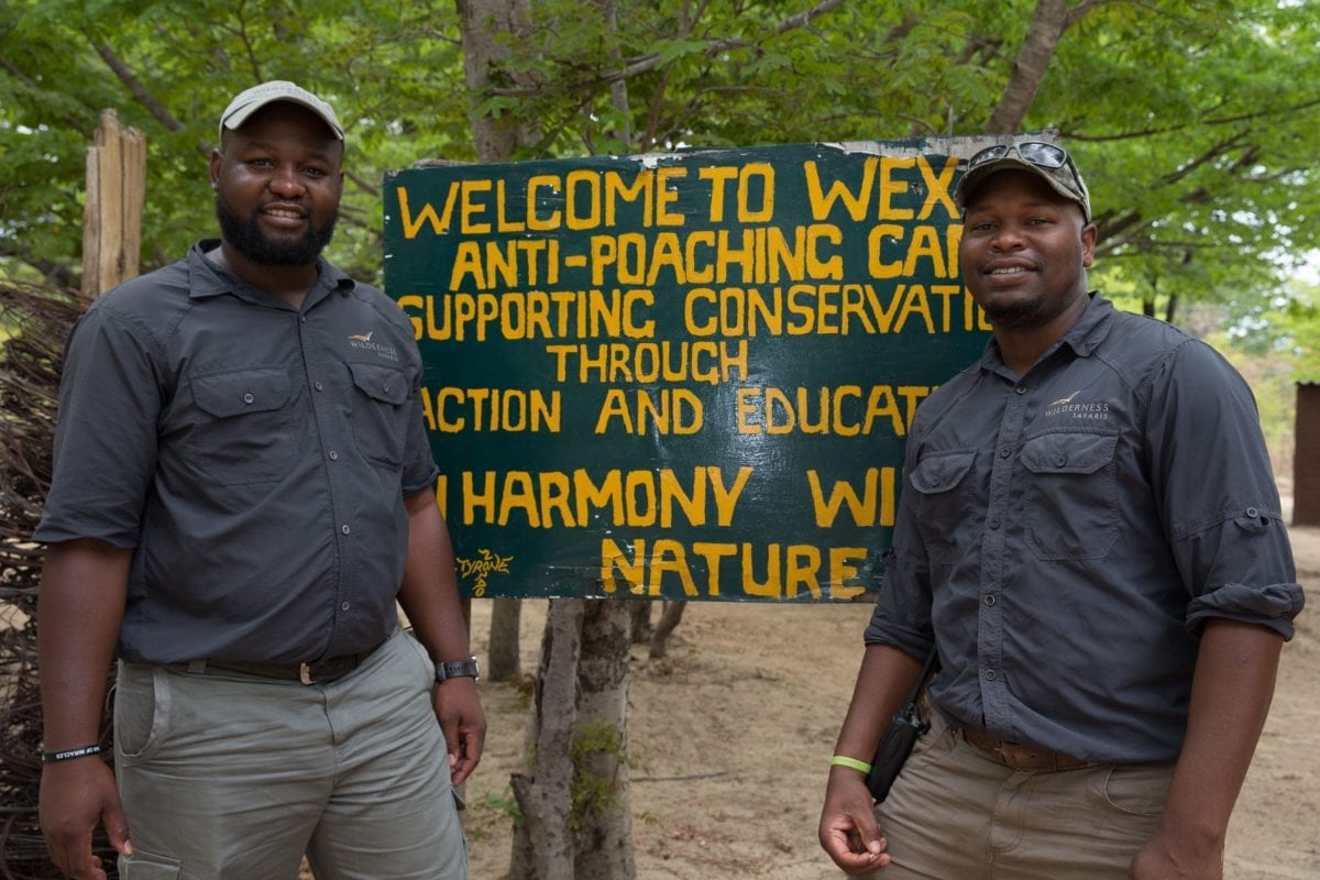 Two of the Wilderness Safaris Scorpion Anti-poaching team standing either side of the camps welcome sign - Zimbabwe