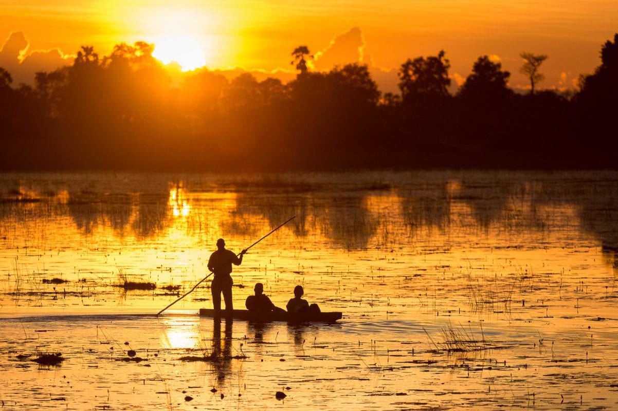 Bright orange sunset behind couple in a mokoro - Okavango Delta